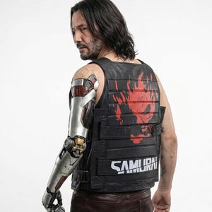 May include: Black leather vest with the word "SAMURAI" in white block letters. The vest has a red graphic on the back. The person in the image has a cybernetic arm.