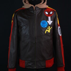 K&ouml;nnte beinhalten: Braune Lederjacke mit beigefarbener Kapuze und roten und gelben Akzenten. Die Jacke hat einen Spider-Man-Aufn&auml;her und andere bunte gestickte Designs. Die B&uuml;ndchen und der Bund sind rot, und die Jacke hat einen durchgehenden Rei&szlig;verschluss.