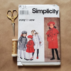May include: A Simplicity sewing pattern for children's coats. The pattern is for sizes BB (baby) and includes three different styles: a red coat with a cape, a white coat with a hood, and a black and white checkered coat. The pattern is labeled "easy to sew" and includes a spool of thread and a pair of scissors.