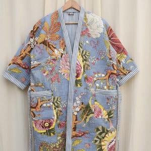 Puede incluir: Bata acolchada azul claro con un estampado floral y de fauna. La bata tiene mangas cortas, dos bolsillos y un ribete a rayas. La bata mide aproximadamente 140 cm de largo.