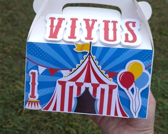 May include: White circus-themed gift box with a handle, featuring a red and white striped tent, balloons, and the word "VIYUS" in red letters. The box has a blue background with starbursts.
