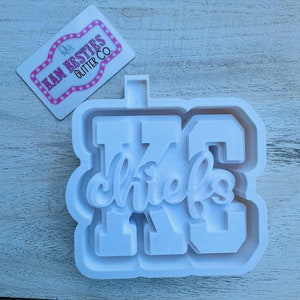 May include: White plastic mold for making a cookie or cake decoration. The mold is shaped like the letters "KC" with the word "chiefs" inside the "C".