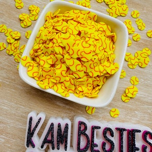 May include: A white bowl filled with yellow and orange softball-themed confetti. The bowl is sitting on a wooden surface. The text "I AM BESTIES GLITTER CO" is visible in the bottom right corner of the image.