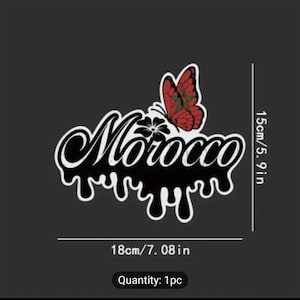 May include: Black and white sticker with the word "Morocco" in a dripping font. A red butterfly with the Moroccan flag on its wings is above the word. The sticker is 5.9 inches tall and 7.08 inches wide.