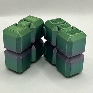 Può includere: Un giocattolo fidget verde e viola fatto di plastica. Il giocattolo è composto da più cubi che possono essere ruotati e ribaltati.