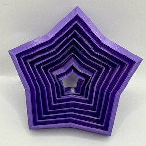 Può includere: Un set di sei tagliapasta a forma di stella di diverse dimensioni, di colore viola.