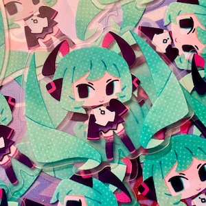 Peut inclure: Plusieurs autocollants transparents représentant un personnage de dessin animé aux cheveux turquoise, avec des détails noirs et une tenue violette et blanche. Les autocollants ont une finition brillante et sont disposés sur une surface à motifs.
