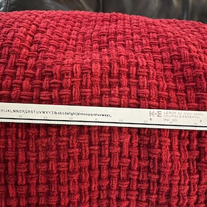Op de afbeelding: Een witte Leroy 61 liniaal met zwarte markeringen en tekst, inclusief letters en cijfers, ligt op een getextureerd rood geweven oppervlak. De liniaal heeft een schaal en de tekst "KEUFFEL & ESSER CO."