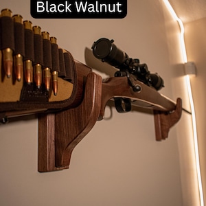 Op de afbeelding: Een geweer met een richtkijker gemonteerd op een zwarte walnoten houten wandhouder. Een bandolier met kogels is naast het geweer gemonteerd. De tekst "Black Walnut" staat in de afbeelding.