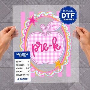 May include: A clear DTF transfer sheet featuring a pink and white gingham apple graphic with the text pre-k in pink script. The design is framed by a scalloped border with stars and includes a size chart listing infant 3 inches to adult 12 inches.