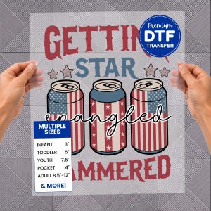 May include: A DTF transfer sheet featuring the text GETTING STAR spangled HAMMERED in red and blue. The design includes three beverage cans decorated with American flag patterns of stars and stripes, along with a size chart listing infant 3 inches, toddler 5 inches, youth 7.5 inches, pocket 4 inches, and adult 8.5 to 12 inches.