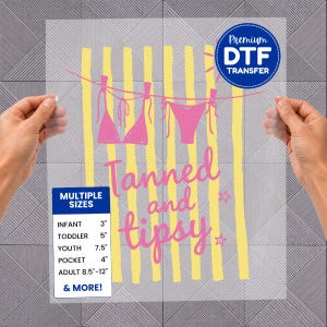 May include: A clear DTF transfer sheet with a pink bikini design hanging on a yellow striped background. The text "Tanned and tipsy" is in pink script. Includes size options: infant 3", toddler 5", youth 7.5", pocket 4", and adult 8.5"-12".
