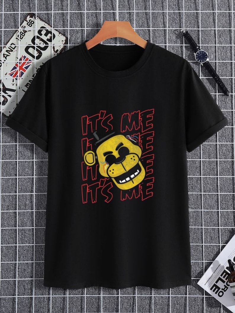 Puede incluir: Camiseta negra con un personaje de dibujos animados amarillo que lleva un sombrero de copa y el texto "It's Me" repetido en rojo.