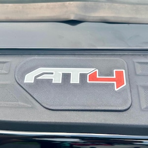 May include: Close-up of a black surface with the white and red letters "AT4". The letters are outlined in white. The image is taken from a slightly elevated angle.