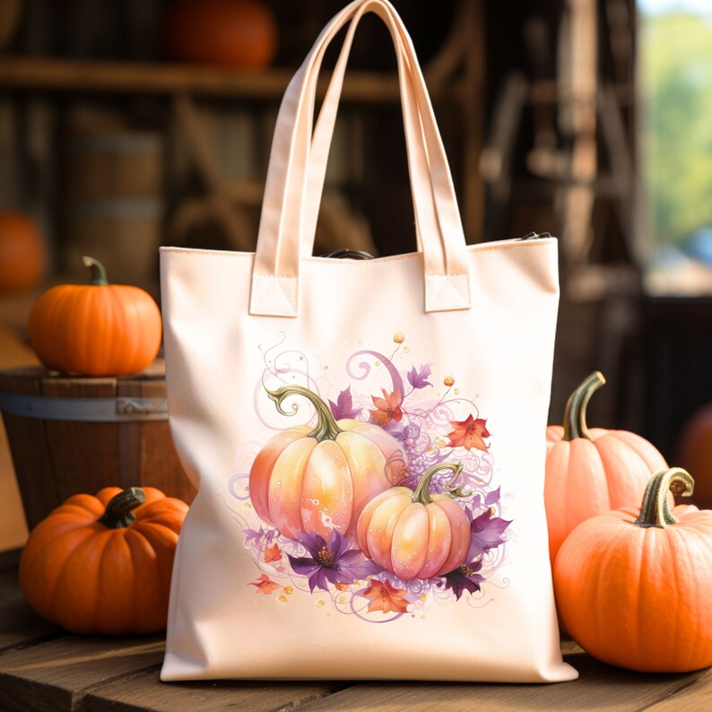 May include: A pink canvas tote bag with a design of three orange pumpkins with purple flowers and leaves. The pumpkins are arranged in a cluster with the largest pumpkin in the back and the two smaller pumpkins in front. The design is surrounded by a swirl of pink and purple.