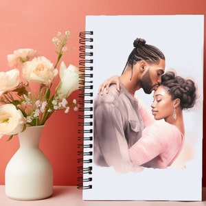 Puede incluir: Un cuaderno con espiral con una ilustraci&oacute;n en acuarela de una pareja abraz&aacute;ndose. El hombre besa la frente de la mujer. El cuaderno est&aacute; colocado junto a un jarr&oacute;n blanco con rosas y vegetaci&oacute;n color melocot&oacute;n.