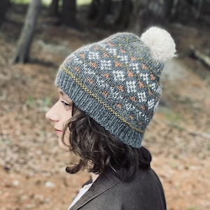 May include: A gray and orange knit beanie with a white pom pom. The beanie has a geometric pattern.