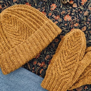 Puede incluir: Gorro y mitones de punto amarillo mostaza. El gorro tiene un borde acanalado y un patrón de chevrón texturizado en la corona. Los mitones presentan un diseño de chevrón similar. El conjunto está hecho de un hilo suave y cálido.