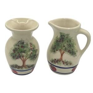 Puede incluir: Dos jarrones de cerámica blanquecina. Uno es una jarra pequeña con asa y pico, el otro es un jarrón con una abertura ancha. Ambos presentan un diseño pintado a mano de un árbol con frutos rojos y hojas verdes.