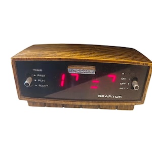 Puede incluir: Reloj despertador digital Spartus vintage con acabado de vetas de madera. El reloj muestra números digitales rojos y tiene función de repetición. Cuenta con perillas de control para la hora y la alarma.