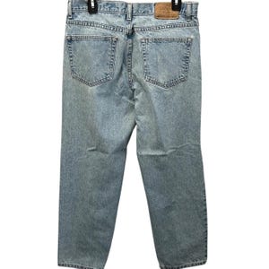 May include: Light wash denim jeans with a classic five-pocket design. The jeans have a straight leg cut and a faded appearance, with a leather patch on the back waistband. The jeans are hanging on a black hanger.
