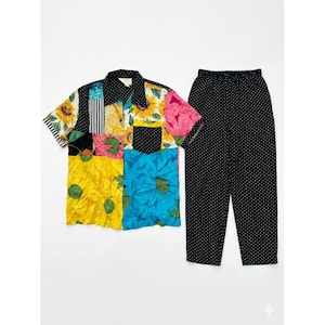 Puede incluir: Un conjunto de camisa de retazos colorida con mangas cortas y cuello negro, junto con pantalones negros con lunares blancos. La camisa presenta patrones florales y geométricos en varios colores.