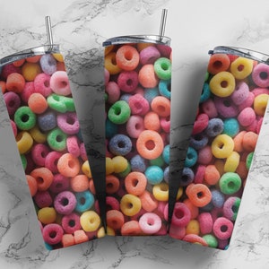 Puede incluir: Tres vasos de acero inoxidable con anillos de cereales coloridos impresos en el exterior. Los vasos tienen tapas y pajitas.