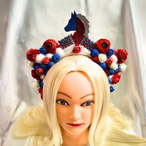 Könnte beinhalten: Ein dekoratives Kopfstück mit einer Pferdesilhouette und floralen Details. Das Kopfstück ist mit roten, weißen und blauen Blumen und Perlen verziert. Die Pferdesilhouette ist rot, blau und silber.