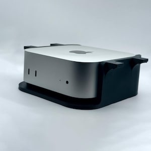 May include: A silver Mac mini computer with a black stand. The computer has a small Apple logo on the top.