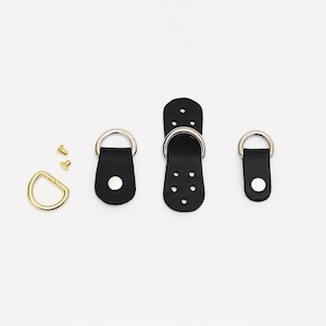 May include: A collection of black leather hardware components with silver metal D-rings and gold-colored screws. The set includes D-rings, leather straps, and a connecting piece, ideal for crafting or bag making.