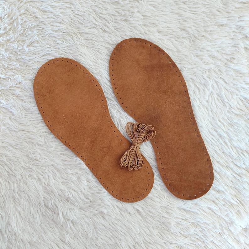 May include: Two brown leather insoles with stitched edges and a bundle of brown thread. The insoles are oval-shaped and designed to fit the inside of a shoe. The thread is tied in a small bundle.