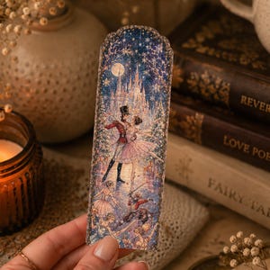 Könnte beinhalten: Ein rechteckiges Lesezeichen mit einer detaillierten Illustration einer Ballettszene mit Schloss, Vollmond und Sternenhimmel. Das Kunstwerk zeigt Tänzer in Kostümen, darunter einen Soldaten und eine Ballerina, vor einer winterlichen Kulisse.