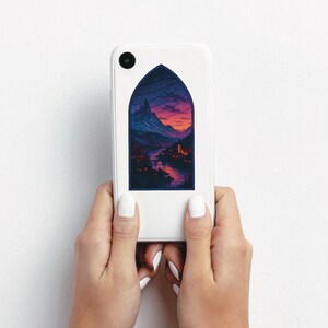 May include: A white phone case featuring a stained-glass style illustration of a mountain landscape at sunset. The design includes a river, buildings, and a starry sky, all within an arched frame.