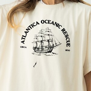 May include: A white t-shirt with a black graphic of a ship and the text "Atlantica Oceanic Rescue Circa 1850".