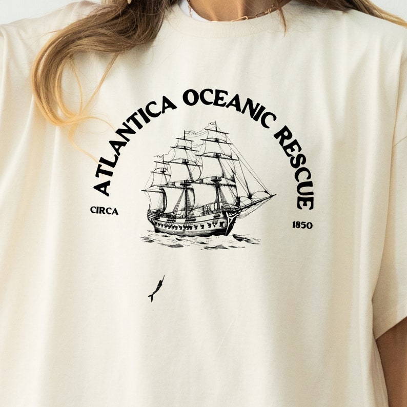May include: A white t-shirt with a black graphic of a ship and the text "Atlantica Oceanic Rescue Circa 1850".