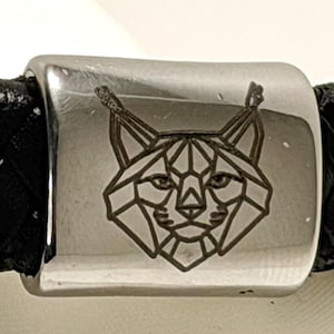 May include: A black braided leather bracelet with a silver clasp. The clasp has a geometric lynx face design. The bracelet is a stylish accessory, suitable for everyday wear.
