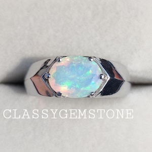 May include: A silver ring with a white opal gemstone set in a bezel setting. The ring has a wide band with a slightly rounded top.