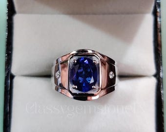 May include: A silver-toned ring with a large, rectangular, deep blue gemstone at the center. The ring has a two-tone design with a rose gold-colored band and two small, clear accent stones on each side of the main stone. The text "Classygemstone" is visible.