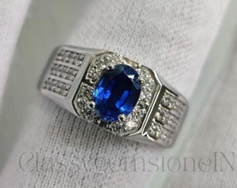 May include: A silver ring with a large, oval, deep blue gemstone at the center, surrounded by smaller, clear stones. The ring has a rectangular design with additional small stones on the sides. The text "ClassygemstoneIN" is visible.
