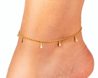 May include: A gold-colored anklet with dangling charms. The delicate chain features small, teardrop-shaped pendants and other decorative elements. The anklet is worn on an ankle, with a white background.