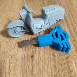 Könnte beinhalten: Ein graues 3D-gedrucktes Modell eines Rollers und ein blauer 3D-gedruckter Schlüssel mit einem Dollarzeichen-Design.