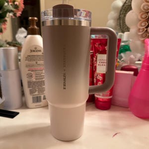 Puede incluir: Un vaso t&eacute;rmico Stanley + Starbucks con asa. El vaso tiene un degradado de color, que va del beige claro en la base al marr&oacute;n m&aacute;s oscuro en la parte superior. Incluye una pajita transparente y una tapa marr&oacute;n.