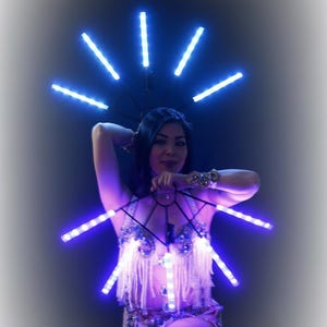 May include: A woman wearing a belly dance costume with integrated blue LED lights. The costume includes a bra, a skirt, and a headpiece, all adorned with bright blue lights. The lights create a radiant effect, perfect for stage performances.