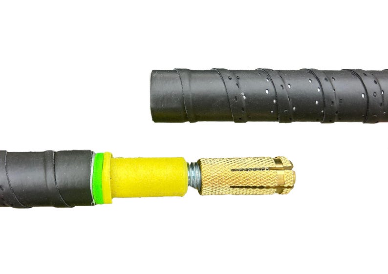 Op de afbeelding: Een zwarte handvat met een gele en groene schuimrubberen inzet en een goudkleurige metalen anker. De handvat heeft een getextureerd oppervlak en kleine perforaties. De onderdelen zijn gescheiden.