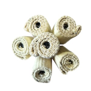 May include: A top-down shot of six rolled beige fabric pieces, forming a circular arrangement. Each roll has a dark centre and a woven texture. The tightly wound rolls display the fabric's construction.