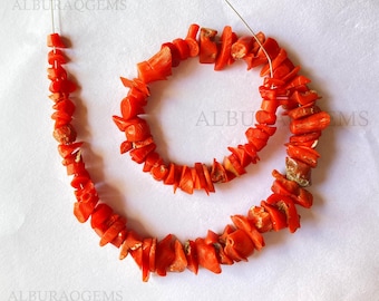 May include: A strand of vibrant red coral beads, strung on a thin wire. The coral pieces are irregular in shape, showcasing a natural, organic aesthetic. The beads are a bright, saturated red, perfect for jewelry making.
