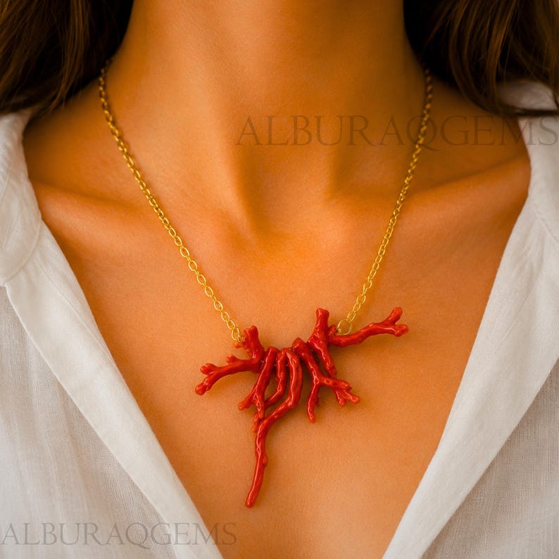 Puede incluir: Un collar con un colgante de rama de coral rojo vibrante de forma org&aacute;nica, suspendido de una delicada cadena de metal dorado. El colgante consta de varios segmentos de coral interconectados que se abren en una formaci&oacute;n natural.