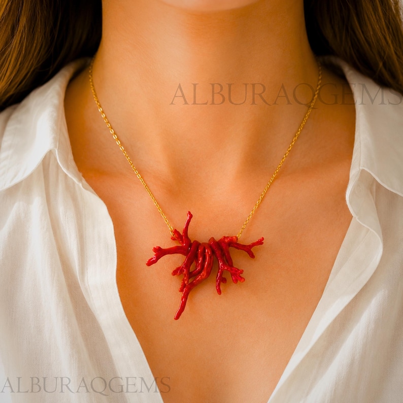 Puede incluir: Un collar con un colgante de coral rojo vibrante en forma de ramas, suspendido de una delicada cadena dorada. El colgante consta de varios segmentos de coral org&aacute;nicos y texturizados agrupados, creando un punto focal natural y ramificado.