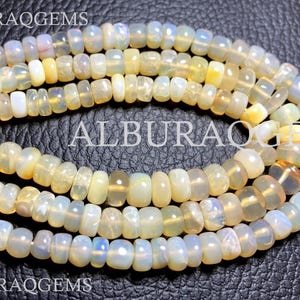 May include: A strand of white and yellow opal beads. The beads are round and have a smooth, polished finish. The beads are strung on a clear thread and are arranged in a loose, flowing pattern.