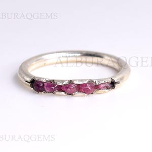 May include: A silver band ring with a row of small pink gemstones set into the band.